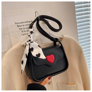 Macro shot of black leather handbag featuring red heart buckle and silk scarf handle detail