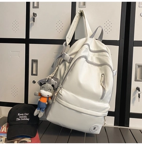 Close-up of a cream nylon backpack with multiple zipper pockets and cow plush charm