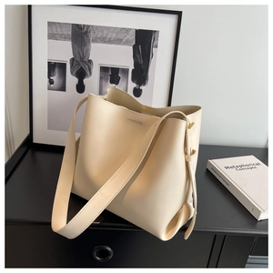 Detail of beige leather bucket bag featuring a side drawstring knot and wide shoulder strap