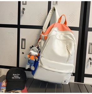Detail view of white and orange nylon backpack with a cute cow plush pendant decoration