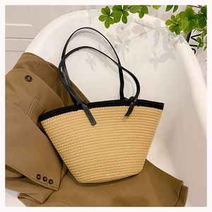 Detail view of a beige woven tote bag with black trim and slim shoulder straps