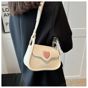 Detail of cream crossbody bag with pink heart decor worn by a model in a black suit