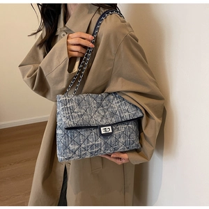 Side view of a blue quilted denim shoulder bag with silver chain and metal turn-lock