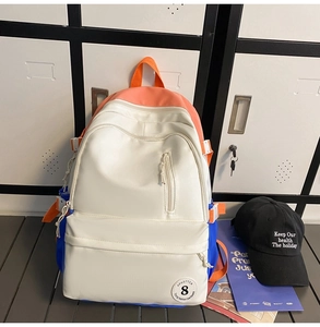 Detail of multi-color backpack with cream, orange, blue panels and circular logo patch