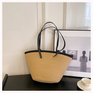 Detail of beige woven tote bag featuring black leather handles and textured straw material