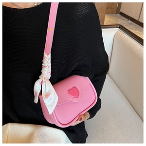 Close-up of pink heart-shaped crossbody bag with decorative silk scarf on shoulder strap