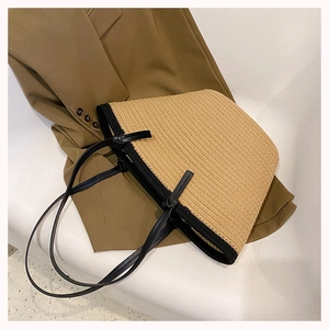 Detail of woven straw tote bag with black handles on a brown blazer for summer style