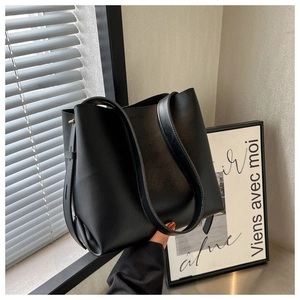Close-up of matte black bucket bag with wide straps and metal buckle details