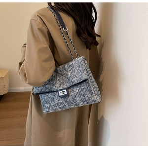 Detail of blue quilted denim bag with silver chain strap and metal lock closure