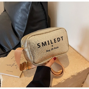 Detail of golden crossbody bag with wide strap on stone surface with French book