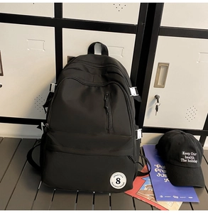 Detail of black nylon backpack featuring front zip pocket and side straps with white buckles