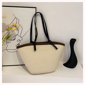 Close-up of beige woven tote bag with brown trim and knotted black straps on display