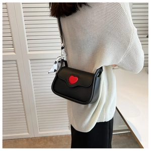 Detail of a chic black leather crossbody bag featuring a bold red heart and silk scarf