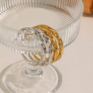 Polished 18K gold and silver twisted C-shape hoop earrings on a glass rim