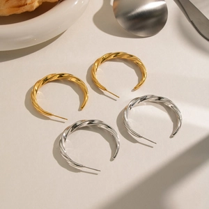 Twisted C-shape hoop earrings in 18K gold and silver finishes with a minimalist metal texture