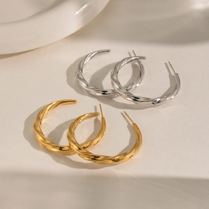 Detail of twisted C-shape metal hoop earrings in polished gold and silver finishes