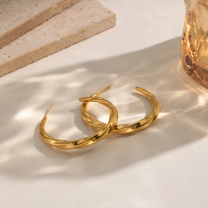 Detail of twisted 18K gold plated C-shaped earrings on stone and glass with ripple shadows