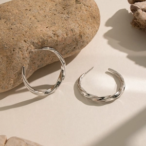 Detailed view of silver twisted C-shape hoop earrings on a textured stone background