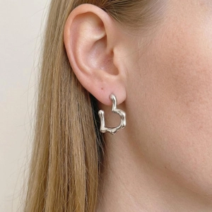 Minimalist silver heart earrings with a melted liquid metal design worn by a model