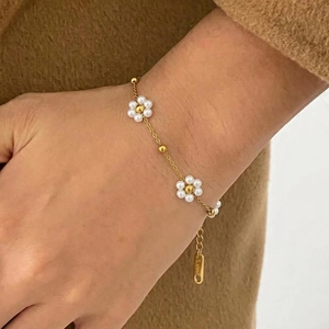 Bracelet élégant en acier doré orné de délicates fleurs en perles blanches sur un mannequin