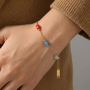 Golden stainless steel chain bracelet with colorful crystals worn on a wrist over a sweater