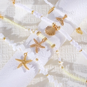 Detalle de tobilleras playeras con dijes de estrella de mar y concha sobre cuentas blancas.