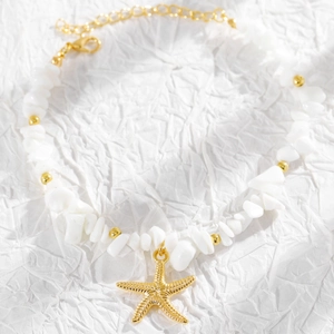 Detalle de cuentas de concha blanca y un colgante de estrella de mar dorada en la tobillera.
