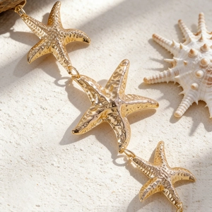Detailansicht goldener Seestern-Anhänger an einer sommerlichen Taillenkette am Strand.