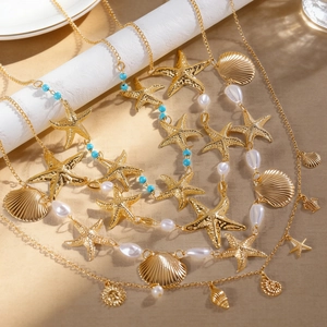 Detailansicht goldener Seestern- und Muschelanhänger an einer Taillenkette im Boho-Stil