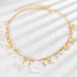 Detailaufnahme einer goldenen Taillenkette im Resort-Stil mit Muscheln, Seesternen und Perlen.