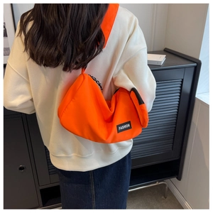 Detail of bright orange nylon crossbody bag with black 'FASHION' label on white hoodie