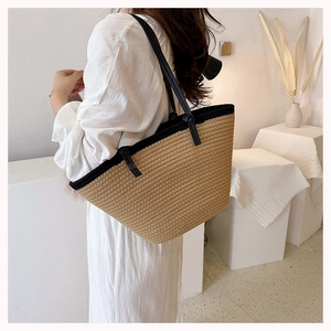 Detail of woven straw tote bag with black shoulder straps and minimalist bicolor design