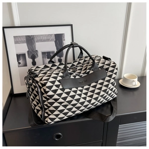 Détail d'un grand sac de voyage en toile à motif géométrique posé sur un meuble d'appoint noir