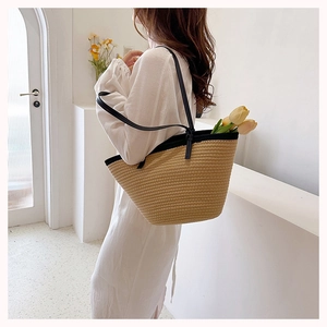 Close-up of a woven straw tote bag featuring contrast black leather handles and trim