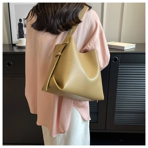 Minimalist khaki leather bucket bag with wide adjustable strap worn by a model