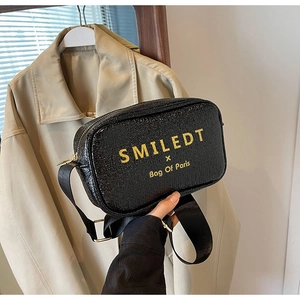 Detail of black crossbody bag with yellow SMILEDT text and adjustable wide strap