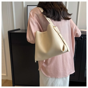 Detail of minimalist cream bucket bag with wide shoulder strap worn by a model