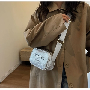 Detail of silver textured mini square bag with wide strap on a model wearing a trench coat