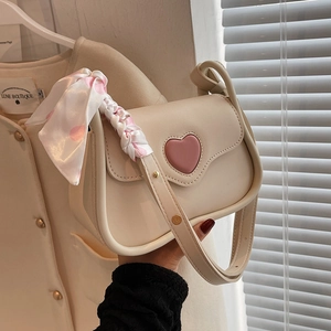 Cream crossbody bag with pink heart and polka dot ribbon handle in a lifestyle setting