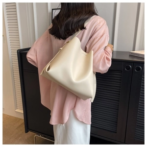 Large beige minimalist tote bag with wide strap worn by model from back view