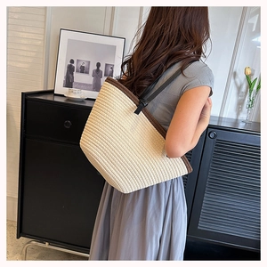 Detail of woven straw tote bag with brown trim and black leather shoulder strap