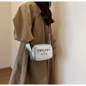 Detail of silver metallic crossbody bag with wide strap and printed logo on the front