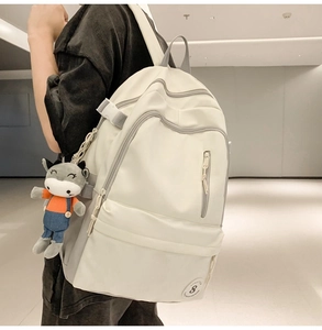Detail view of a large cream backpack with contrast grey zippers and a plush donkey charm