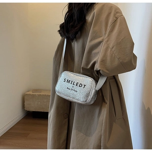 Detail of silver metallic crossbody bag with wide strap and SMILEDT branding text