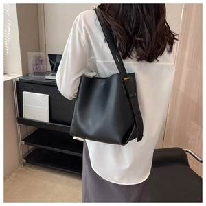 Side view of black leather bucket bag with adjustable strap worn by a model in soft lighting