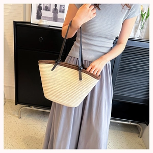Detail of woven tote bag with cream texture, brown trim, and slim black leather handles