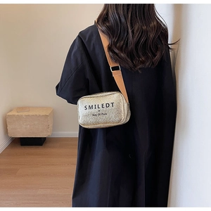 Detail of trendy gold crossbody bag with wide strap on a model wearing a black coat