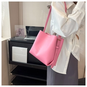 Pink leather bucket bag with wide adjustable strap worn by a model in a minimal setting