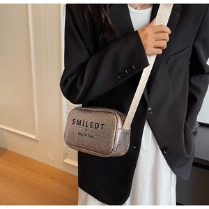 Silver metallic camera bag with wide strap worn with a black blazer and white dress