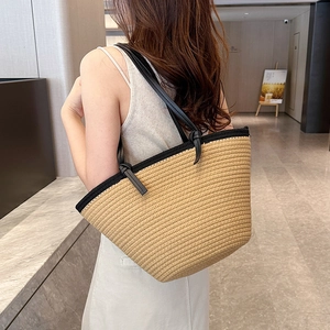 Large khaki woven tote bag with black leather straps and knotted detail in a modern setting